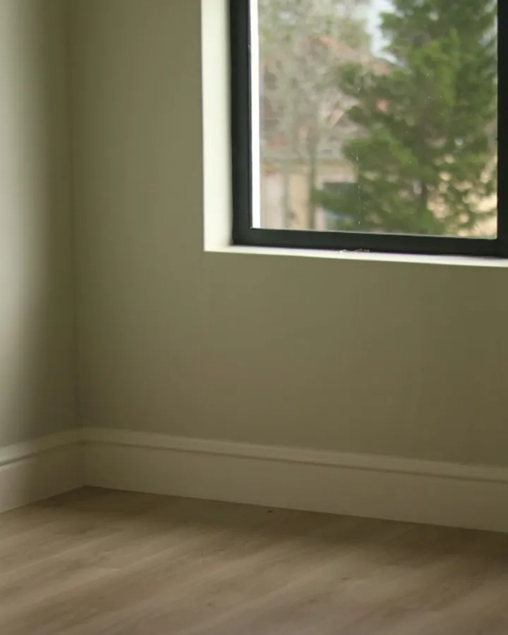Lege kamer met lichtgroene muren, een raam en een houten vloer